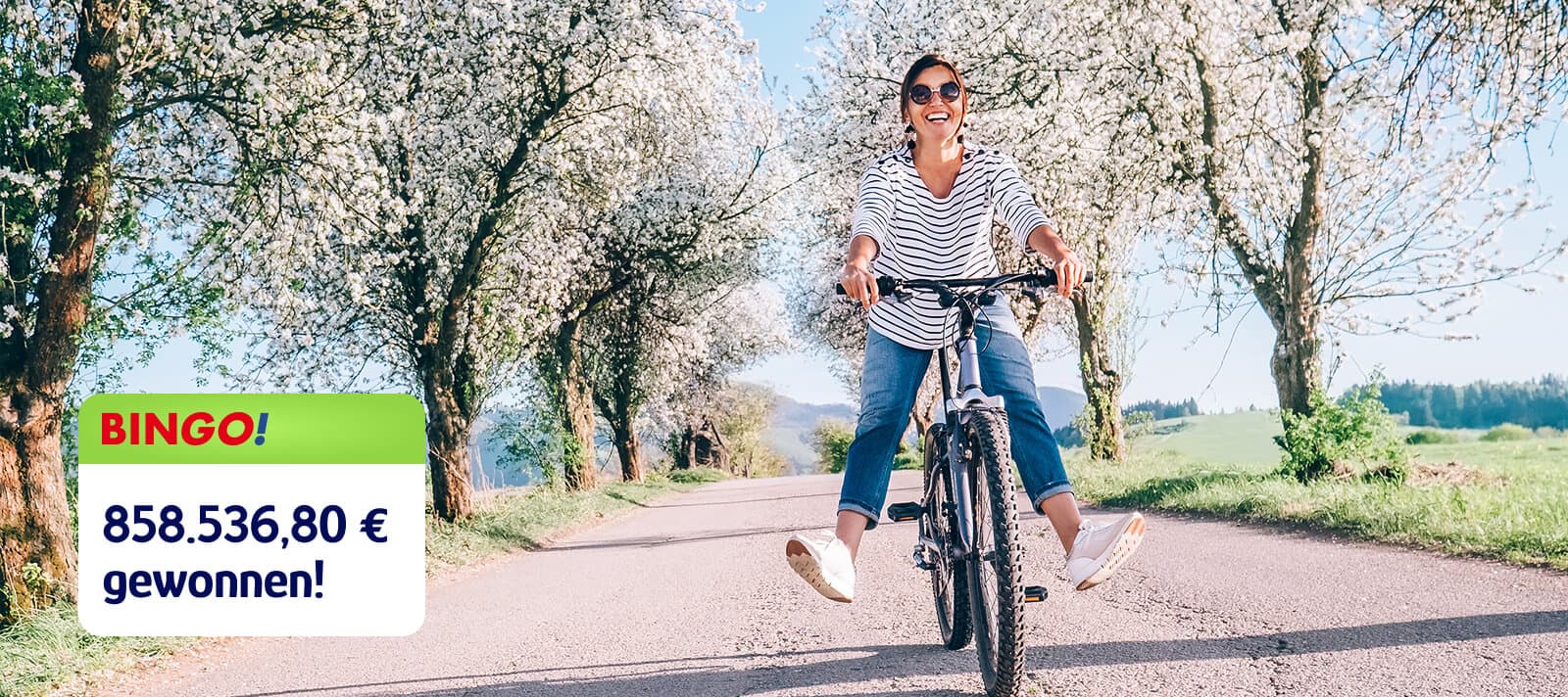 Frau fährt fröhlich Fahrrad unter blühenden Bäumen, trägt eine Sonnenbrille und ein gestreiftes Oberteil, mit eingeblendeter „Bingo!“-Gewinnmeldung über 858.536,80 Euro.
